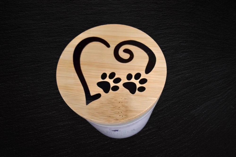 Wooden lid of a candle jar featuring a printed heart outline and two dog paw prints-